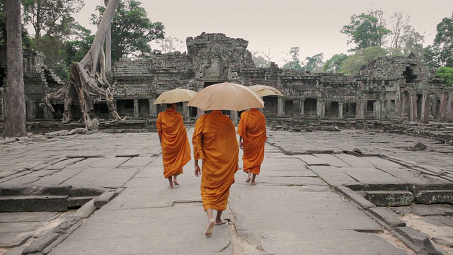 柬埔寨暹粒吴哥窟的僧侣们打着阳伞穿过一座古老寺庙的庭院视频素材