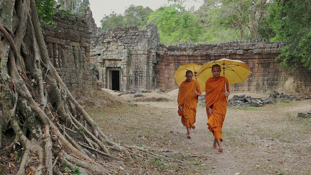 柬埔寨暹粒，佛教僧侣们手拿阳伞穿过吴哥窟一座古老寺庙的庭院视频素材