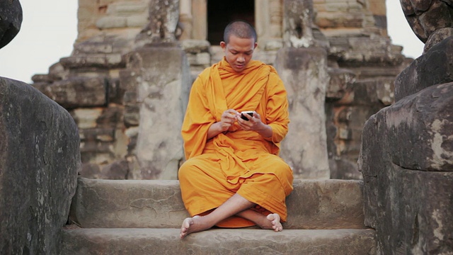 在柬埔寨暹粒吴哥窟(Angkor Wat / Siem Reap)的一座古庙里，一名和尚在智能手机的屏幕上轻触视频素材