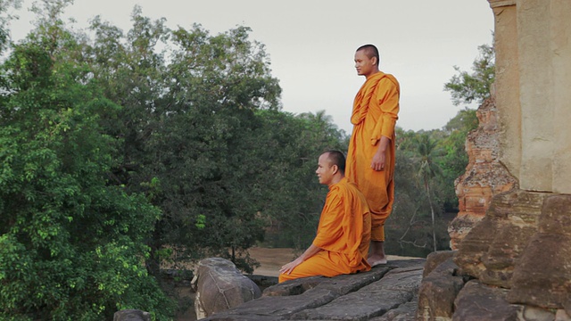 在柬埔寨暹粒吴哥窟的一座古庙里，佛教僧侣们一边聊天一边望着丛林对面的日出视频素材