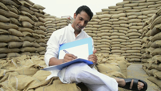 印度哈里亚纳邦古尔冈市，Farmer坐在一堆谷物袋子旁边，制作袋装记录视频素材