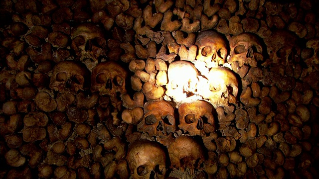 中等近距离手提式倾斜-手电筒照在巴黎一个地下墓穴的墙壁上的头骨和骨头。法国/巴黎视频下载