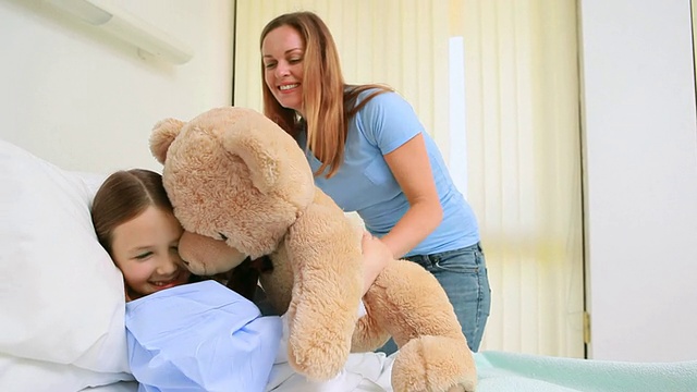 快乐的女人把泰迪熊给一个躺在床上的女孩视频素材