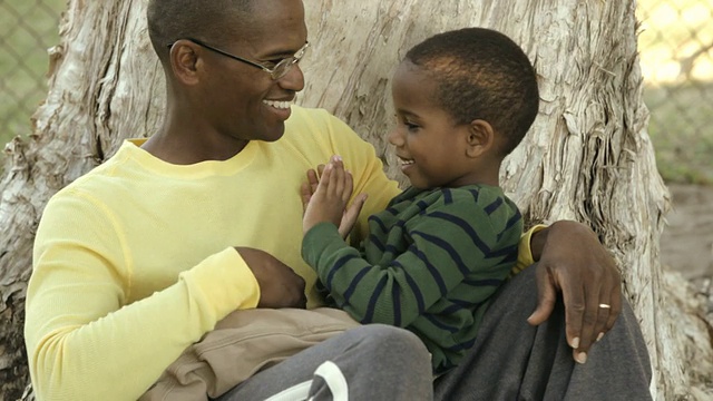 一位非裔美国父亲，儿子坐在他腿上视频素材