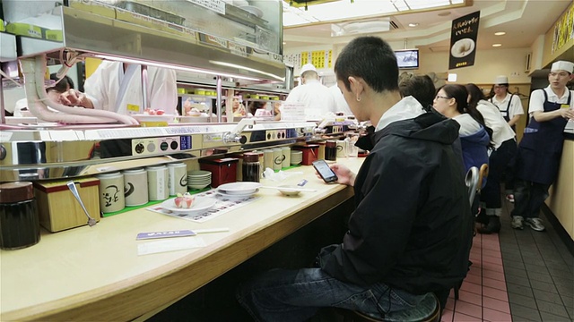 日本东京，一名男子在一家寿司餐厅里使用智能手机视频素材