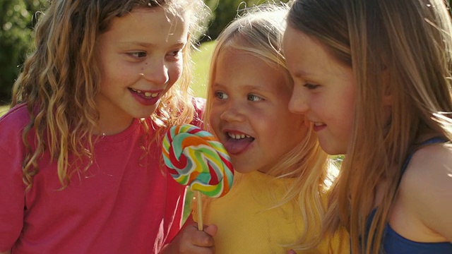 三个孩子在公园舔棒棒糖的慢镜头。视频下载