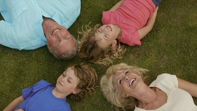 祖父母和孙辈们躺在花园里的草地上。视频素材