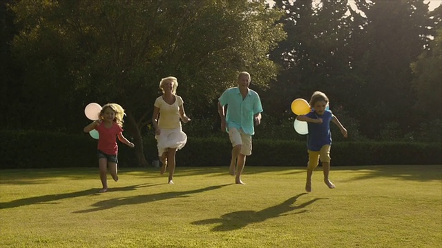 孙辈和祖父母在花园里拿着气球奔向摄像机的慢镜头。视频素材