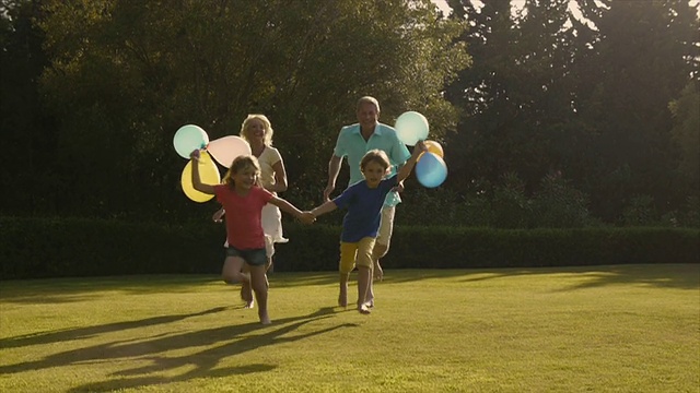 孙辈和祖父母在花园里拿着气球奔向摄像机的慢镜头。视频素材