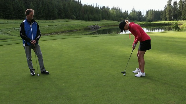 高尔夫球手把球放在果岭，与同伴观看视频素材