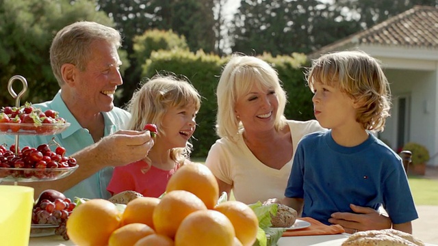 爷爷奶奶和孙子孙女们在花园里玩着，坐在餐桌前吃着食物。视频素材