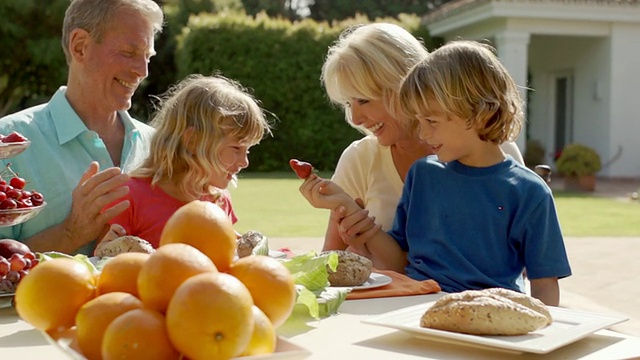 爷爷奶奶和孙子孙女们在花园里玩着，坐在餐桌前吃着食物。视频下载