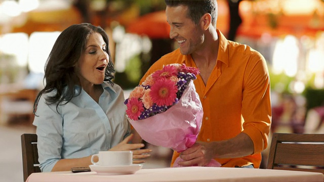 一个年轻人在咖啡馆里送花给一个年轻女子。视频下载