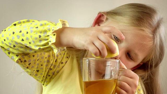 小女孩挤着柠檬，喝着茶。视频素材
