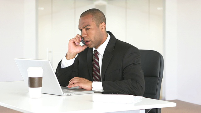 男性主管坐在办公桌前，带着笔记本电脑和手机视频素材