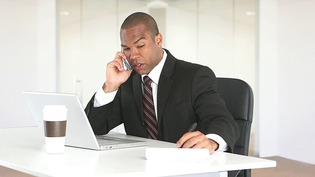 男主管坐在办公桌前，一边用笔记本电脑一边打电话视频素材