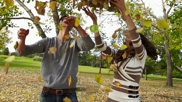 男人和女人在秋天扔树叶玩得很开心视频素材