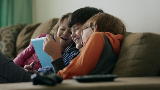 小朋友们坐在沙发上一起看平板电脑，面带微笑视频素材