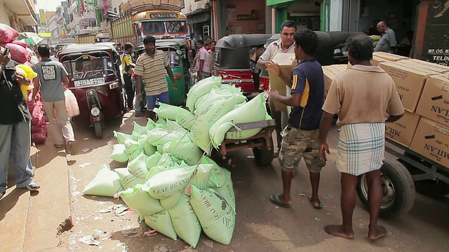 图为斯里兰卡西部省份科伦坡的皮塔市场上，一群男人扛着沉重的货物和经过的送货拖车视频素材