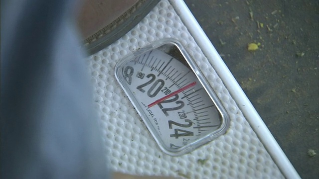 中等近距离手提式——一个男人站在秤上，秤上显示的是220磅。美国加州/视频下载