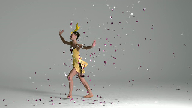 芭蕾舞者跳跃穿过紫色和银色的花朵在她周围飘下来的慢动作视频素材