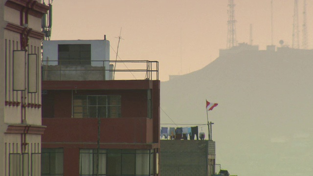 “住宅建筑的屋顶，衣服挂在绳子上，秘鲁国旗，国旗在风中飘扬，后面是山圣克里斯托巴尔，阴天，秘鲁利马。”视频下载