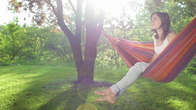 一个年轻女子在树下的吊床上荡秋千视频素材