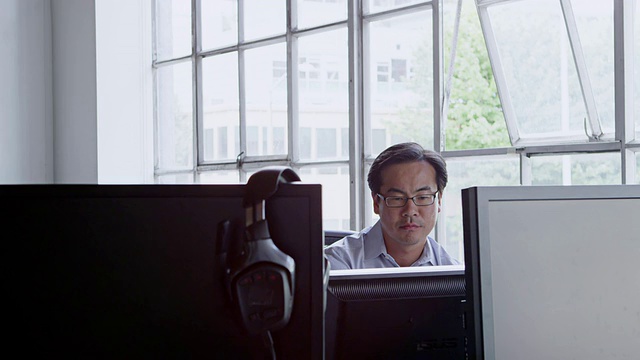 微软商人坐在办公室里，周围都是电脑显示器，望着窗外视频素材