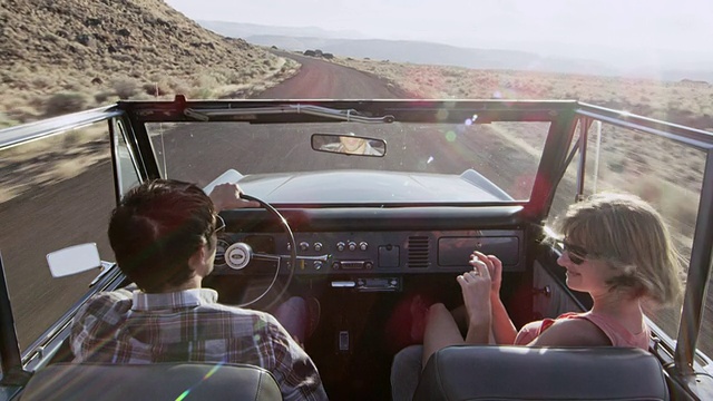 MS年轻夫妇驾驶敞篷车在沙漠道路上的女人用智能手机拍照视频素材