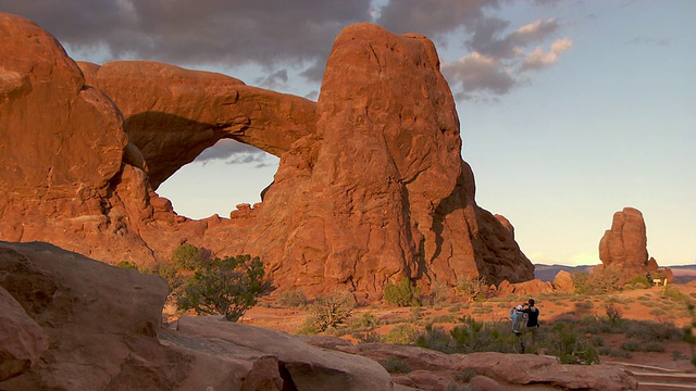 男人和女人徒步旅行在沙漠小径附近南窗拱门在眼镜区域日落-放大视频下载