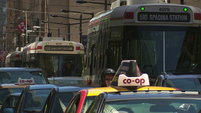 在加拿大多伦多市一条繁忙的街道上，汽车、出租车和有轨电车堵塞了交通。一群人从镜头前走过。视频素材