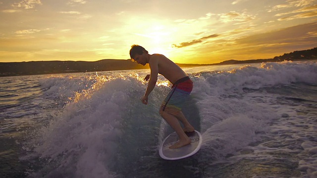日落时分，一个年轻人在小船后面冲浪视频素材