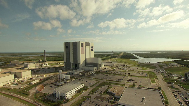 MS AERIAL ZO拍摄于美国佛罗里达州肯尼迪航天中心的车辆组装大楼上的NASA标识和美国国旗，该大楼带有停车场和其他建筑视频素材