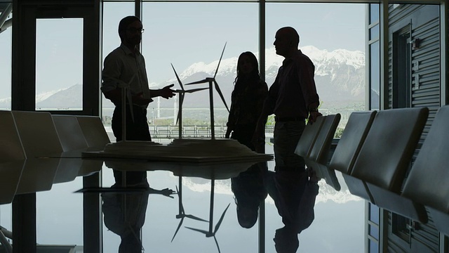 美国犹他州普罗沃，在会议室中摇出商人们看着风力涡轮机模型然后握手的剪影。视频下载