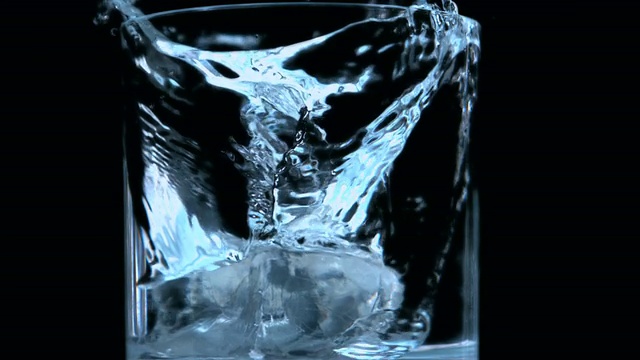 在黑色背景下，两块冰块落入玻璃杯中视频下载