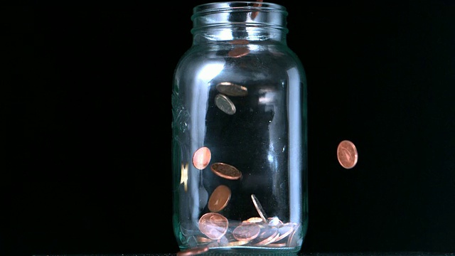 许多硬币倒入玻璃罐中视频素材
