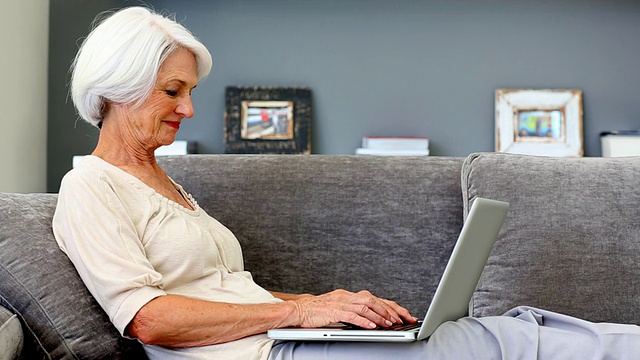 老妇人在沙发上用笔记本电脑视频素材