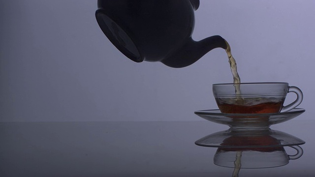 在灰蓝色的背景下，茶壶将茶倒入清澈的杯子中视频下载