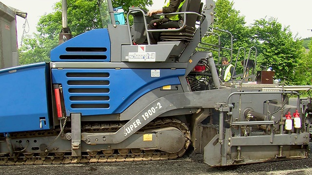 德国莱茵兰-普法尔茨萨尔堡的沥青铺路机正在进行路面重铺和工人们的工作视频下载