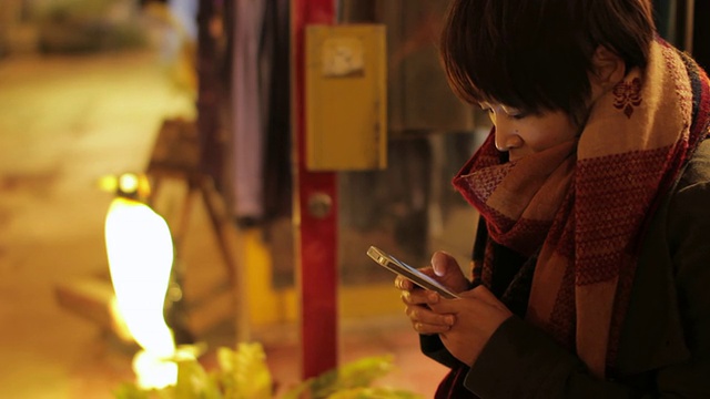 这是一名年轻女性在日本冲绳县中古宿的一家商店前使用智能手机的照片视频购买