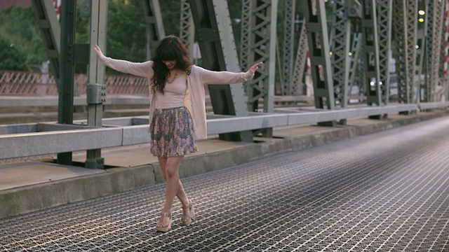 MS TS SLO MO美丽的黑发姑娘沿着桥欢快地走着，而车辆在她身后行驶/美国俄勒冈州波特兰视频下载