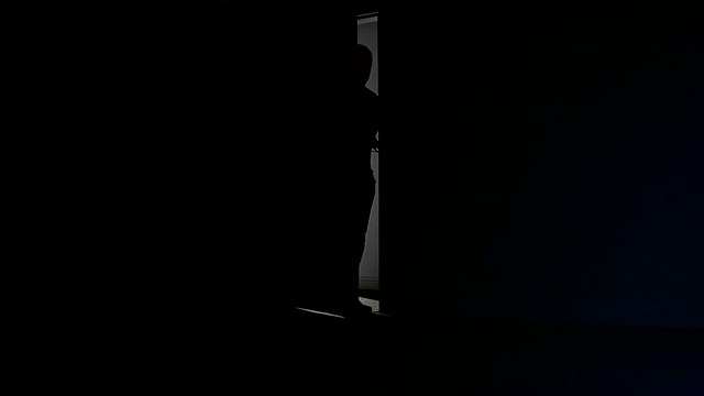 剪影男子打开门，向黑暗的房间里望去。视频下载