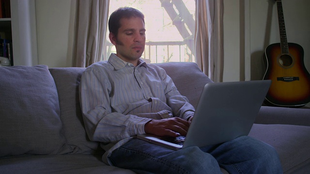 美国纽约，一名男子坐在公寓沙发上用笔记本电脑打字视频素材