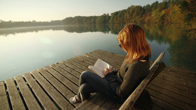 一个年轻女子在湖边的长椅上看书视频素材