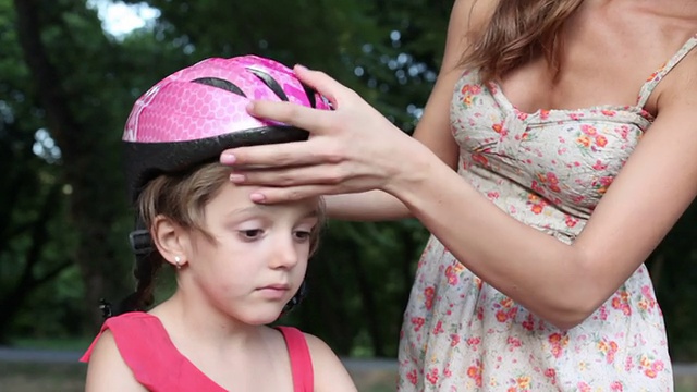母亲帮助女儿戴自行车头盔。视频素材