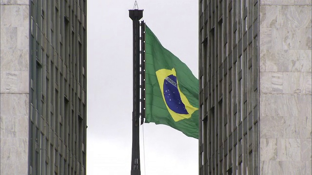 巴西国旗在巴西利亚国会大厦的两座塔楼之间飘扬。高清。视频素材