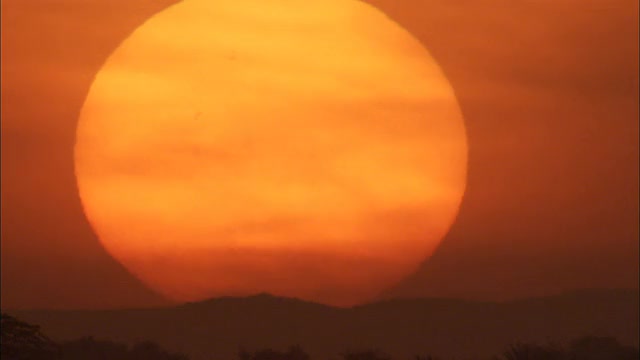 在希巴姆，一个巨大的橙色太阳在低矮的沙漠山丘的剪影后面落下。视频购买