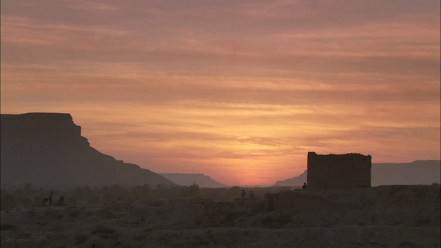 在希巴姆也门，一座多石的沙漠山丘和一座石塔的轮廓映衬着明亮的橙色天空。视频素材
