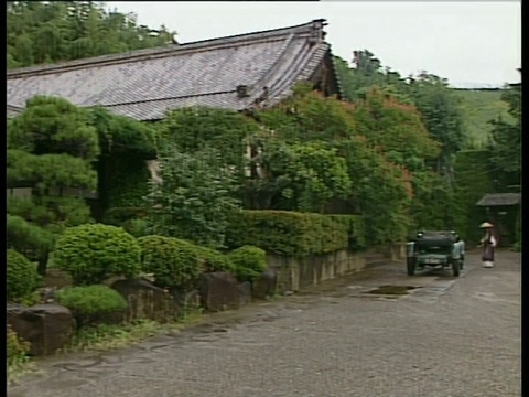 潘右沿着日本房子周围的树木，英国古董车停在外面，路过穿着传统服装的日本人农村日本视频素材
