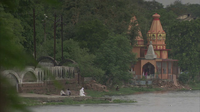 在一条河和两座寺庙式建筑附近，树枝随风摆动。高清。视频下载